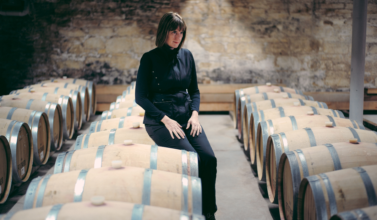 A woman sits on a wine barrel in a cellar